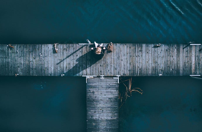 Aerial shot of a girl on a pier establishes she is alone and surrounded by water.