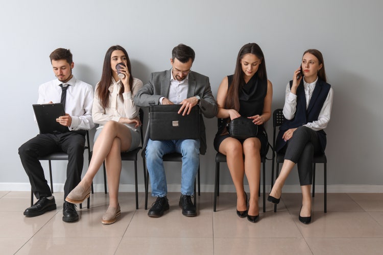 Cinque persone attendono sedute su una sedia prima di un colloquio di lavoro