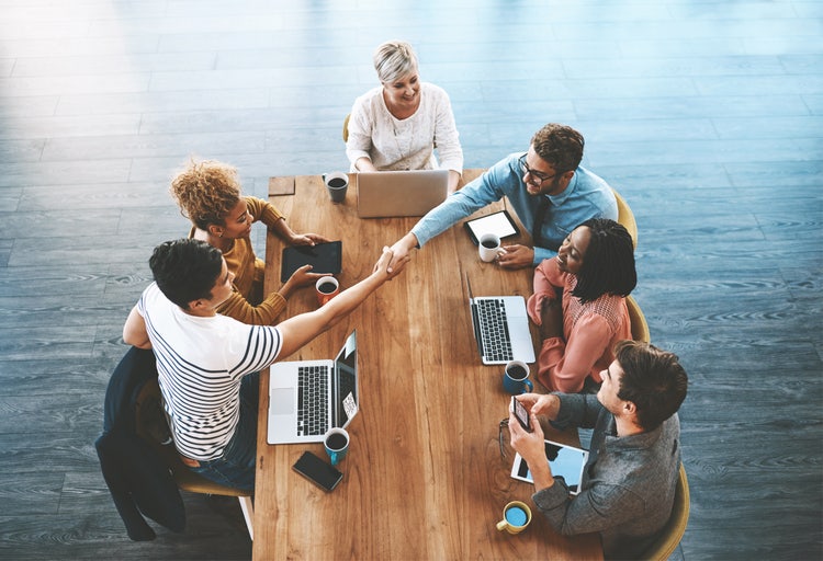 Diverse persone sedute attorno a un tavolo con computer e caffè, due di loro si stringono la mano