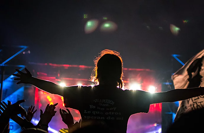 A person with their hands out, sitting on someone's shoulder at a concert