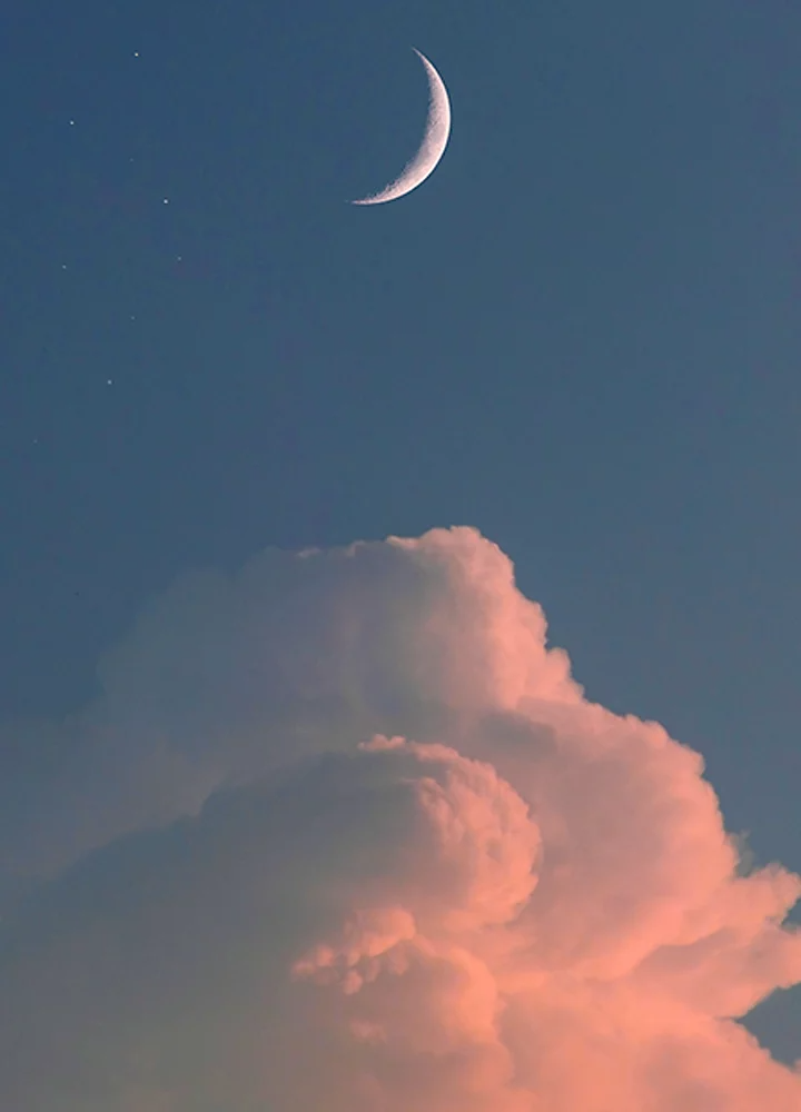 Crescent moon high above a stack of cumulus clouds