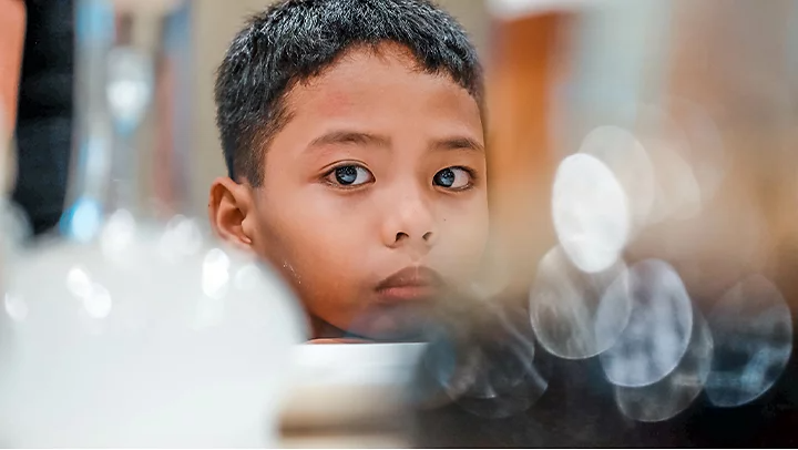 A child posing and staring into the camera with out of focus objects between him and the lens