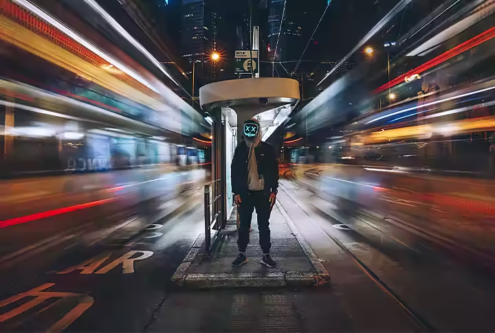 Time-lapse di veicoli sfocati che sfrecciano accanto a una persona in piedi alla fermata dell’autobus.