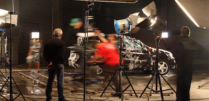 Foto a effetto movimento di produttori che riprendono un’auto sul set.