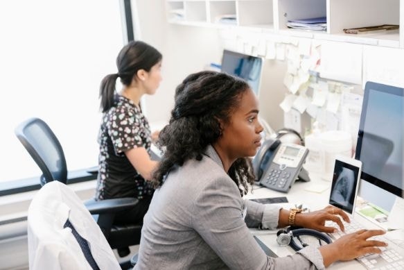 Two health practitioners working at a computer station to type out reports between seeing patients