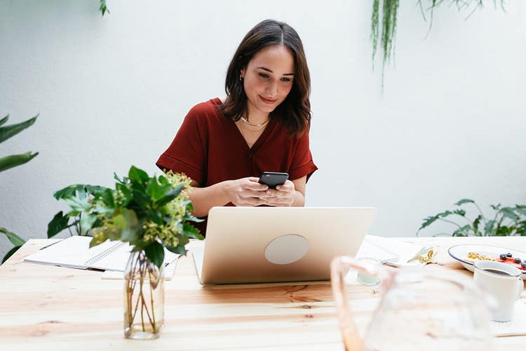 A person reviews a sales contract on their computer while reviewing details on their smartphone