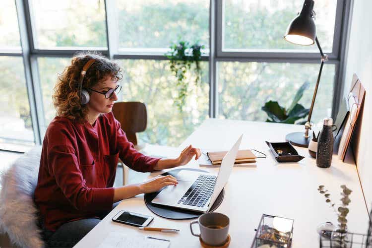 A person sitting at a desk wearing headphones and using their Mac laptop to sign a document