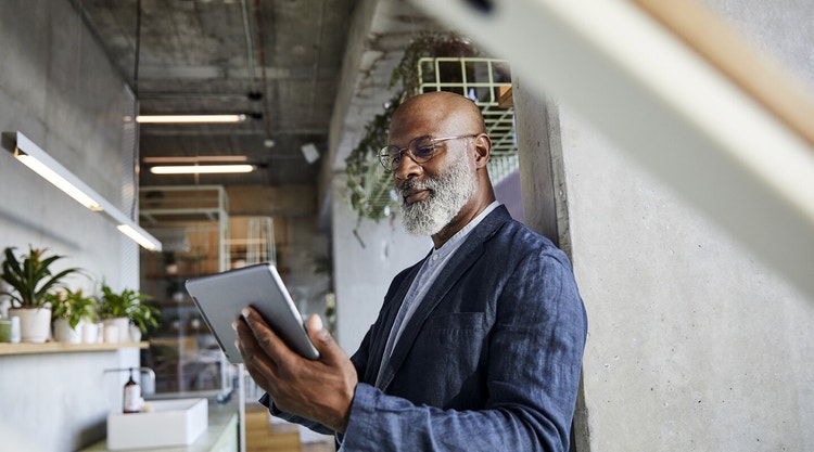 A person leaning against a concrete pillar reviews a sales contract on a tablet