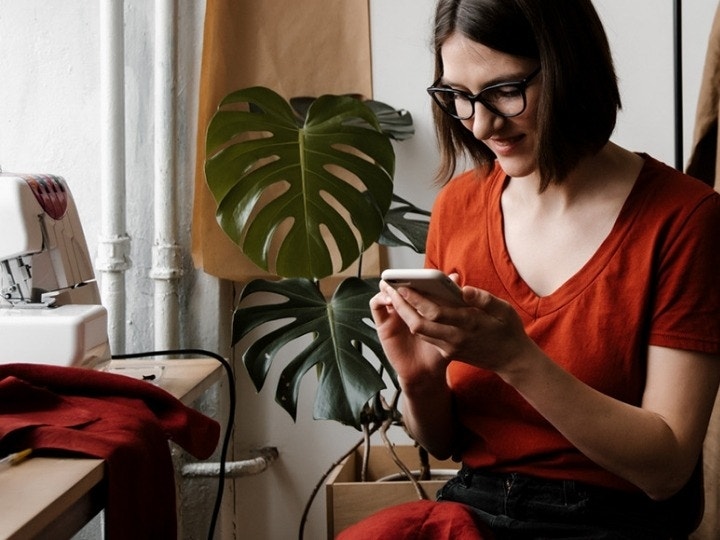 A small business owner looking over an email on their phone while taking a break from sewing their products.