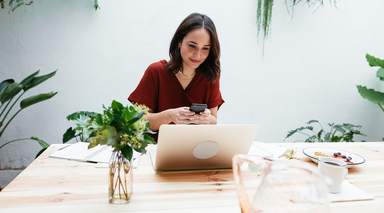 A person reviews a sales contract on their computer while reviewing details on their smartphone