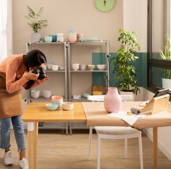 A freelance pottery maker taking eCommerce photos of their latest pastel bowls and a vase