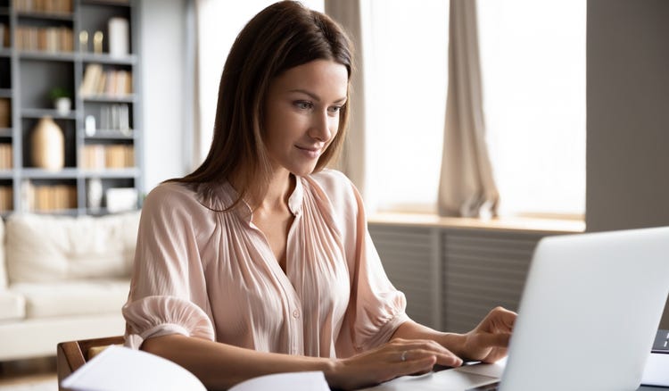 A person writing on a laptop in a sunny room.