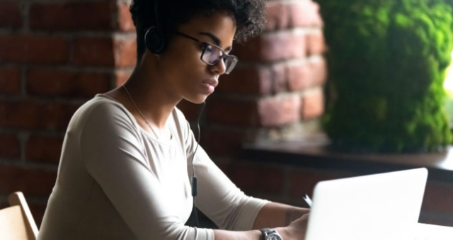 A woman preparing photo lookbooks on a laptop while listening to music outside on a college campus patio