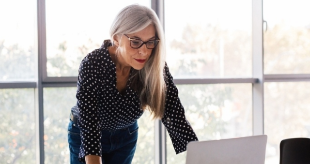 A woman working intently at a laptop while standing as if she is so focused on the work as to not need a chair