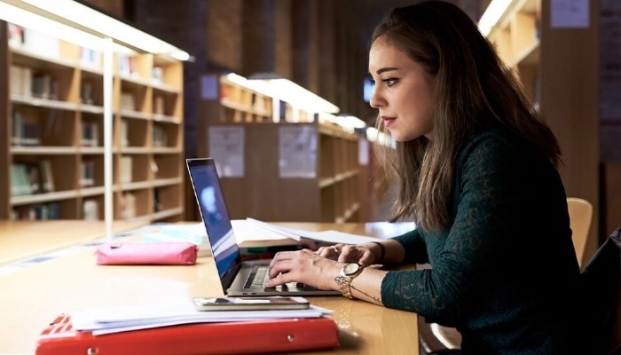 A student sitting in a university library working on a laptop