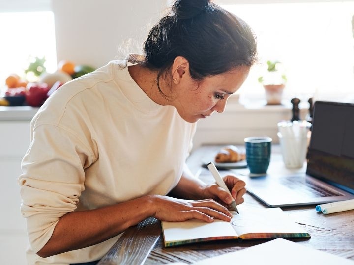 A freelance worker drawing in a notebook and working on a laptop in Adobe Acrobat to read and edit PDFs