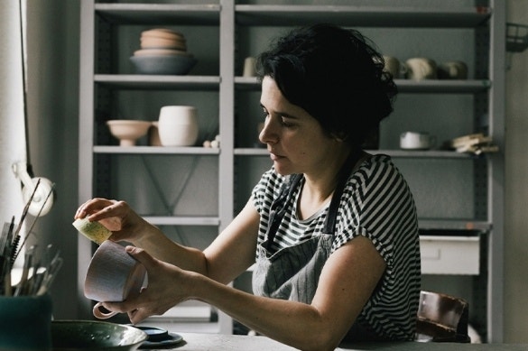 A potter brushing the edge of a clay bowl in their studio