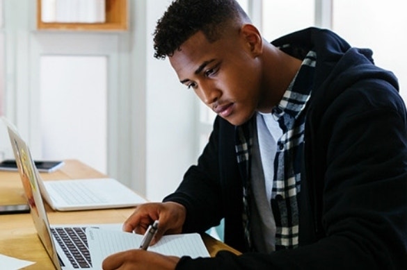 A college graduate using a notebook and their laptop to research job opportunities