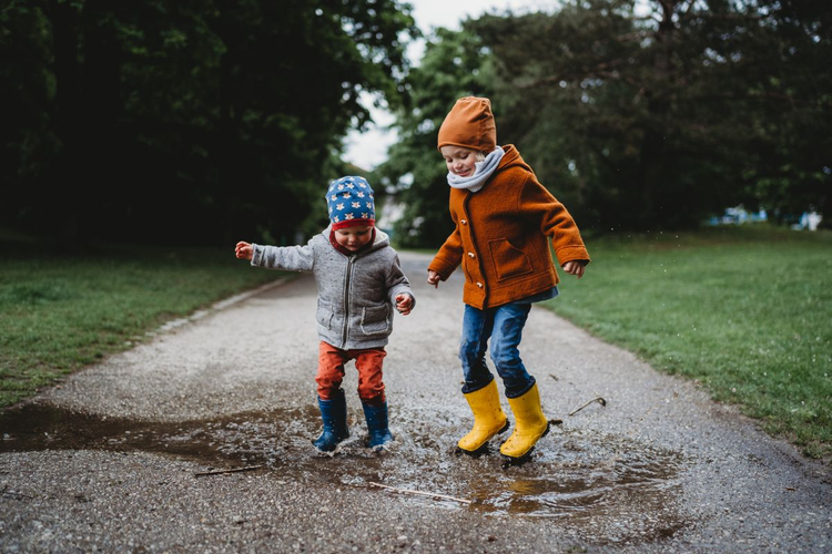 A photo of two children jumping in a puddle.