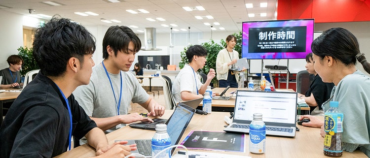 A group of people sitting at a table with laptops Description automatically generated