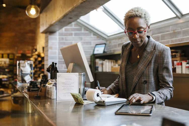 Woman in business attire and red glasses reviewing a contract on a tablet and doing accounting tasks