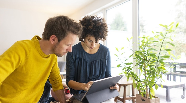 Two potential tenants standing and looking down at a house rental agreement on a tablet device