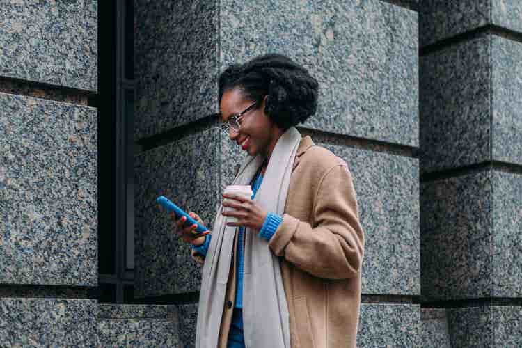 A woman filling out a signature using their mobile phone while holding coffee outside a building