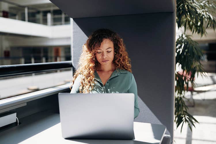 A person sitting at a table in the atrium of a building working on their laptop