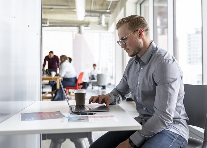 Man with glasses sitting at a desk reviewing an employment contract on a laptop next to his coffee