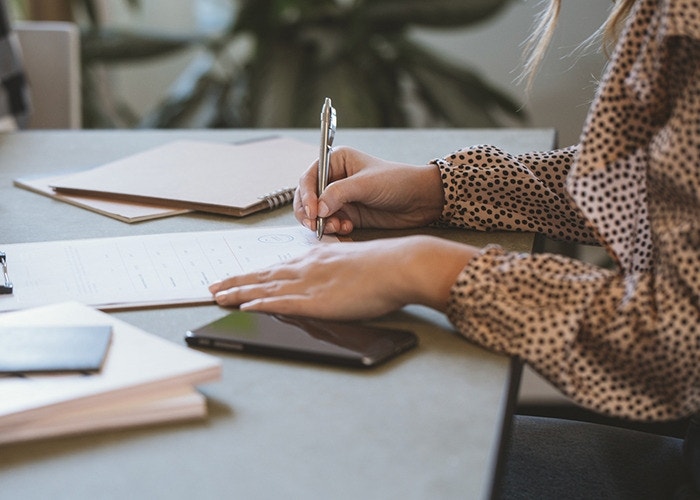 A woman writing a wet signature using a pen on a paper while sitting at their desk