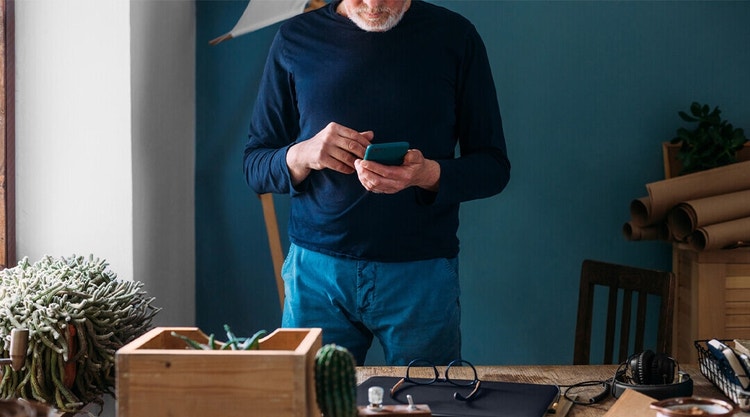 A home buyer standing in front of their desk signing a real estate contract on their mobile phone