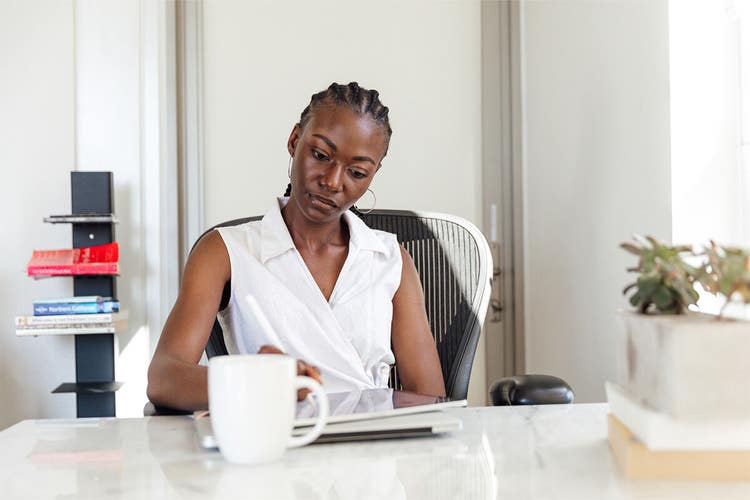 An image of a person sitting at a desk in an office using a tablet with a stylus in their hand.