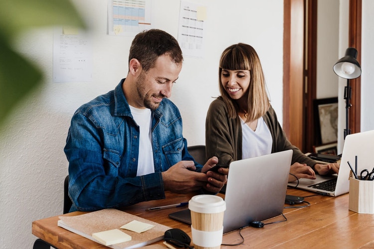 Two people sitting next to each other at a table with their laptops