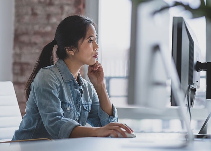 Woman in a denim shirt reviewing an employment contract on a computer monitor