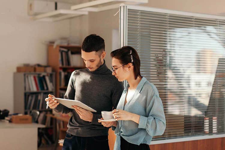 A young man and young woman standing and reviewing a wholesale contract on a tablet together.