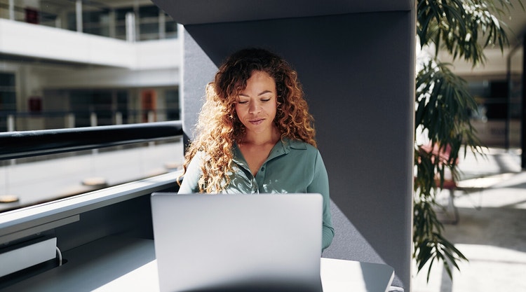 A person sitting at a table in the atrium of a building working on their laptop