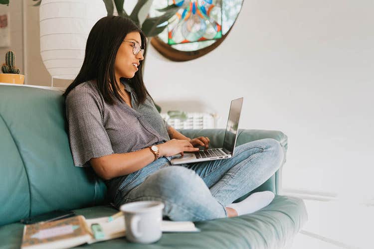 A woman with black hair and glasses on a couch reviewing a purchase agreement on her laptop.