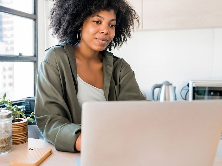 A photo of a person sitting at a counter in a kitchen and working on a laptop computer.