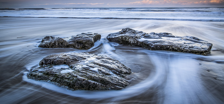 Motion blur of water passing by rocks at the shore