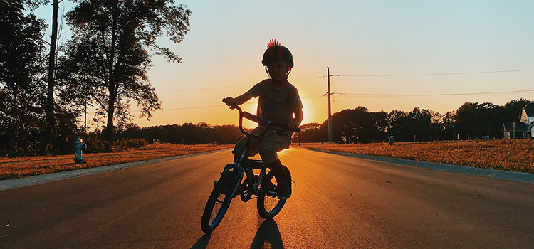 Child riding a bike directly in front of a sun setting placing emphasis on the silhouette of the child