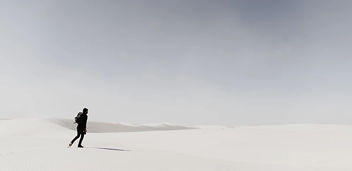 A person wearing black standing in a desert dune