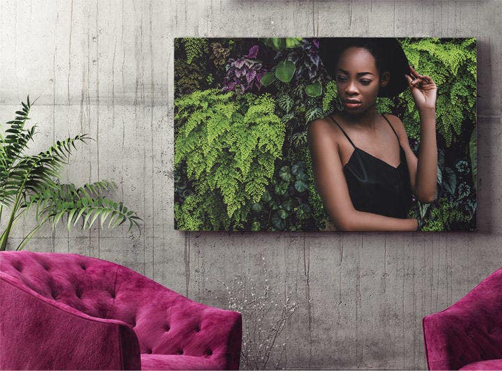 Picture of model in front of new background with green plants placed on a wall behind two fuchsia-colored chairs