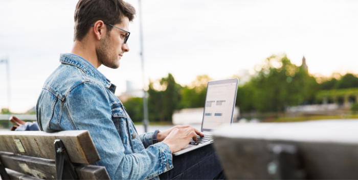 Man sitting on park bench outside using a Mac computer.