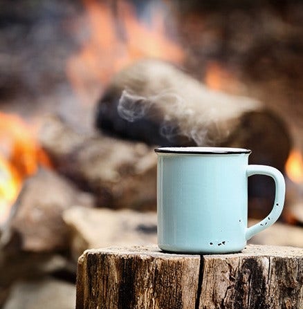 Still-life picture of a coffee cup near a campfire shot with a shallow depth of field