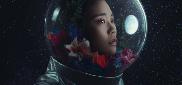 A model posing with an astronaut suit on and their helmet filled with some flower petals in it