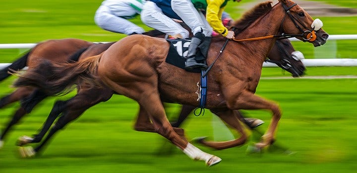 Motion blurred image of horse race with horses and jockeys racing.