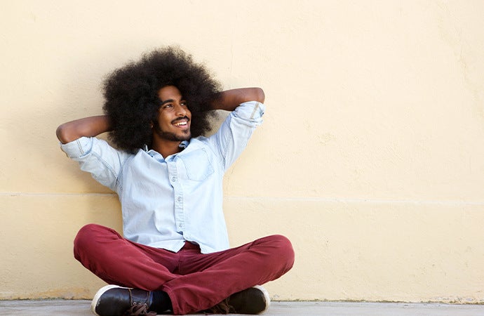 Man sitting down and smiling to the side against tan concrete wall.