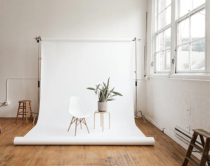 A chair and a plant on top of an end table setup on a white studio backdrop