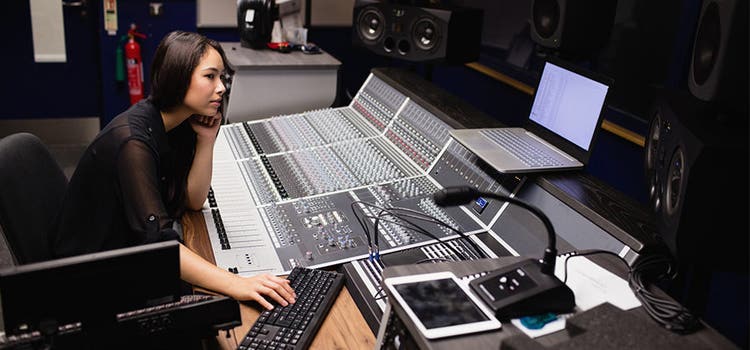 Eine Frau sitzt in einem Tonstudio vor umfangreichem Audio-Equipment