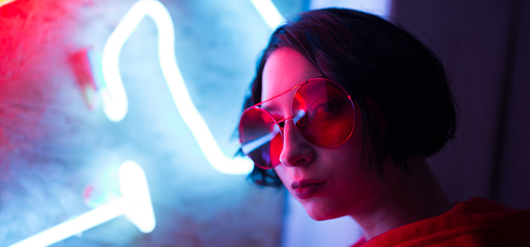 Portrait photo of a person wearing sunglasses standing in front of a neon light